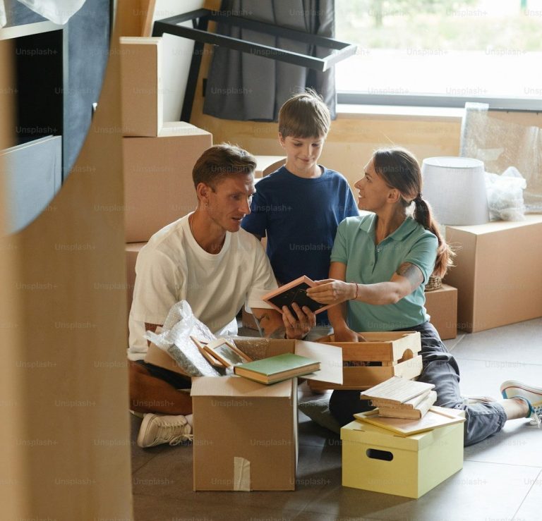ASESOR HIPOTECARIO Familia organizando cajas y libros en una habitación con accesorios de mudanza.