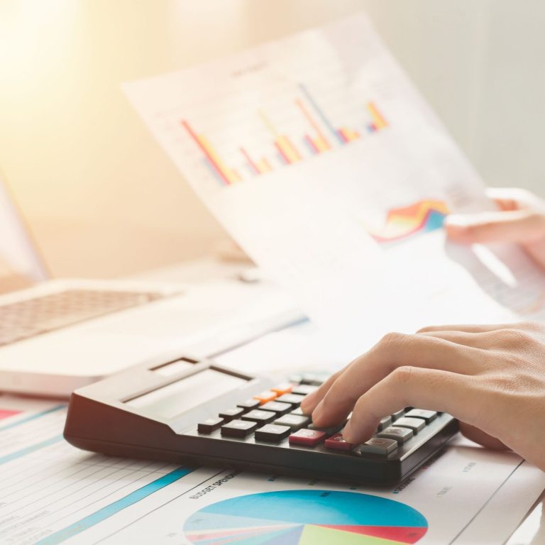 planificación financiera Mano usando una calculadora mientras revisa gráficos y un informe en una mesa para realizar una planificación financiera