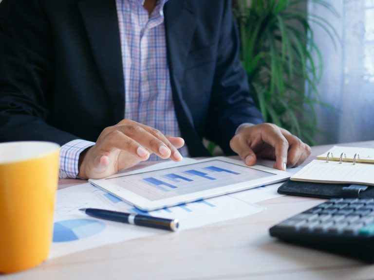 MRP ASESORES Mano usando una tablet sobre una mesa con gráficos, taza y calculadora para analizar los gastos de autónomo